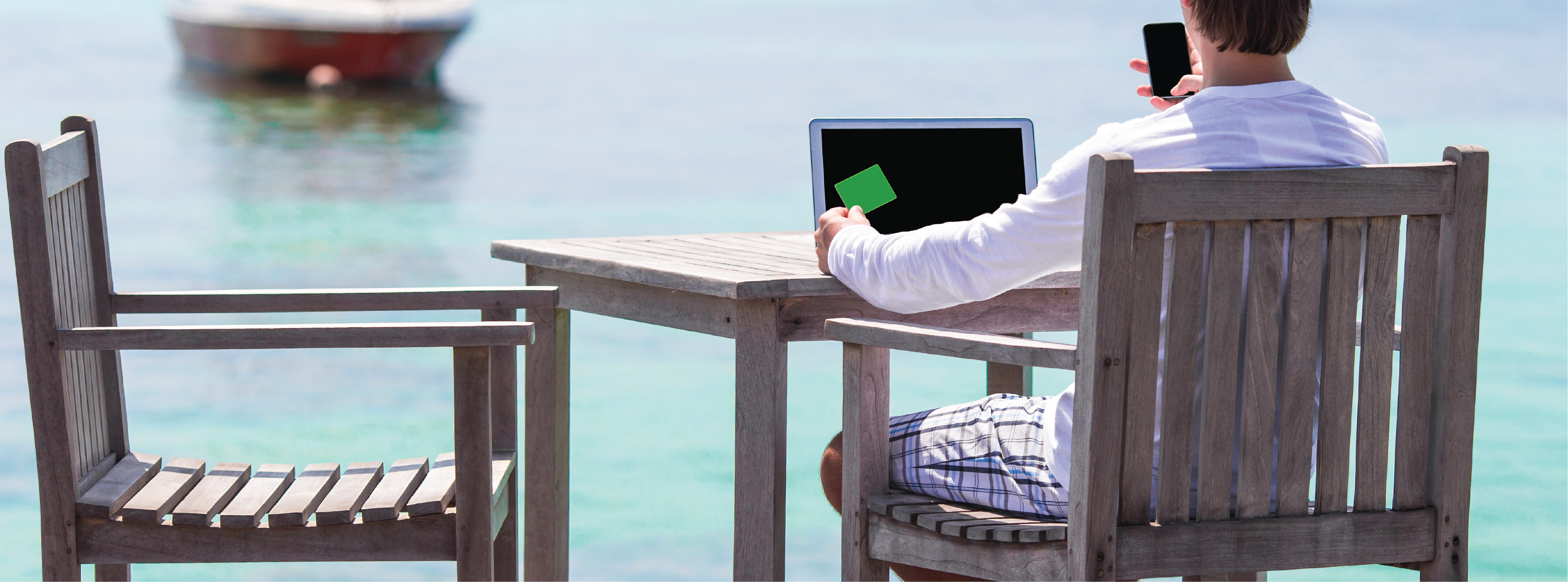 Someone sitting by the water on their computer and phone